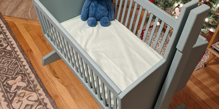 Blue baby cradle with a blue stuffed elephant sitting in the corner of it.